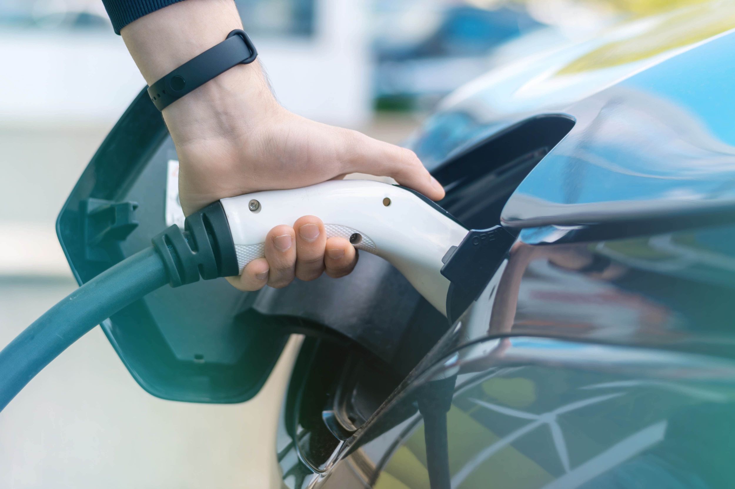 Nahaufnahme von einer Person, die ein Ladekabel an ein Elektroauto anschließt